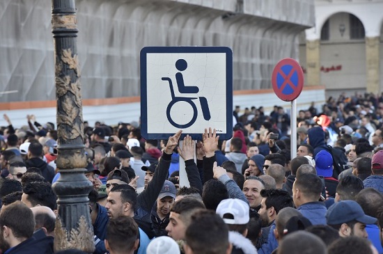 Algerian demonstrators hold a placard with the symbol of a man on a wheelchair (representing their president), during a demonstration against Algeria's president's candidacy for a fifth term, on February 22, 2019 in Algiers. In power since 1999, Bouteflika has used a wheelchair and has rarely been seen in public since suffering a stroke in 2013. - Several hundred demonstrators, in defiance of a ban on protests, rallied in the Algerian capital today against a bid by ailing President Abdelaziz Bouteflika for a fifth term, an AFP correspondent said. (Photo by RYAD KRAMDI / AFP)
